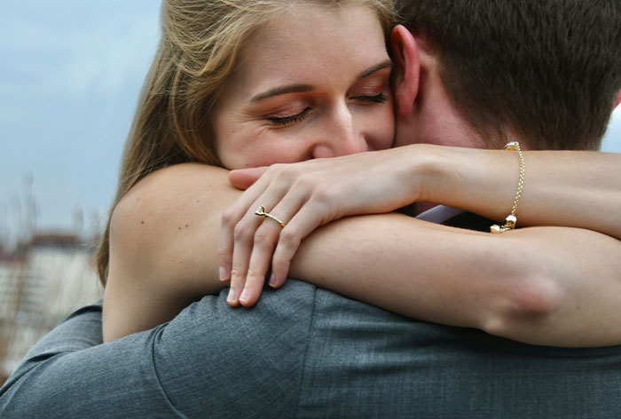 Woman embracing man tightly, showing engagement ring, symbolizing discovery of first cousin engagement after family Christmas.