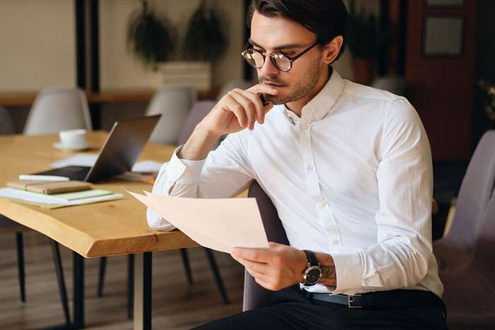 Man in white shirt reviewing prenup document at table, contemplating terms before engagement decision. Man in white shirt reviewing prenup document at table, contemplating terms before engagement decision.