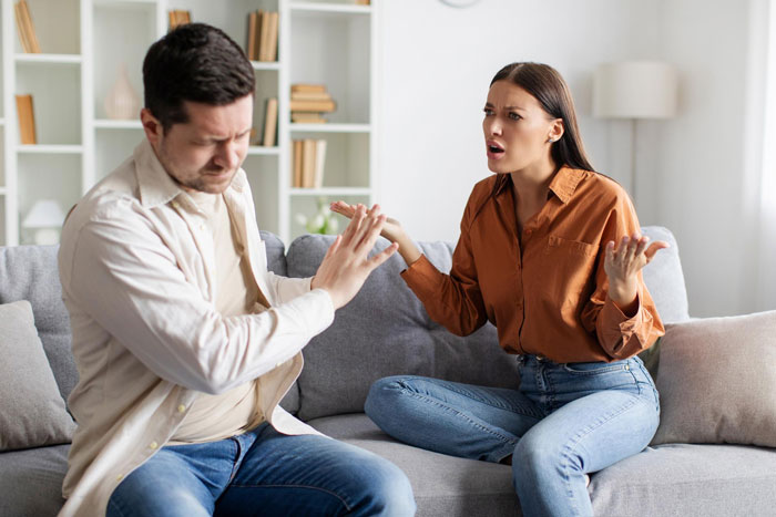 Man refusing to listen while woman argues angrily on couch, depicting bratty teen causing damage and family tension.