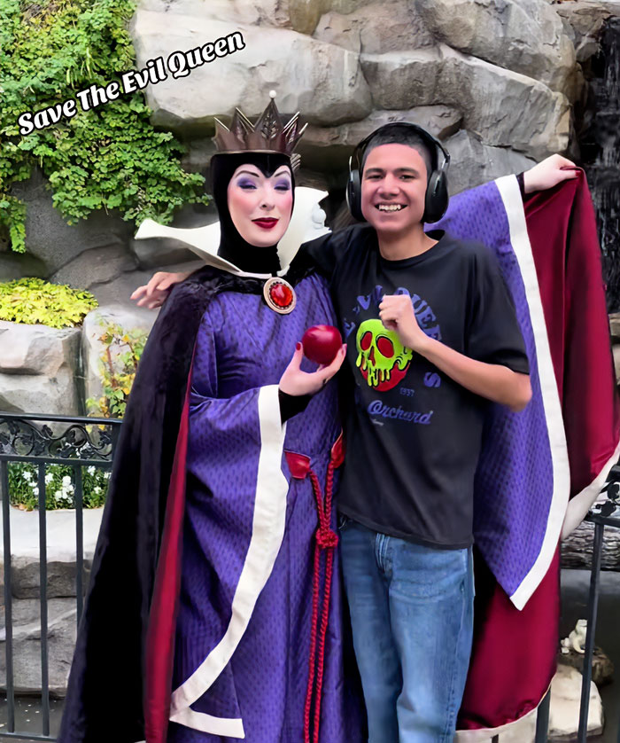 Viral Evil Queen in costume holding an apple, standing next to a smiling young man with headphones outdoors by rocks and greenery.