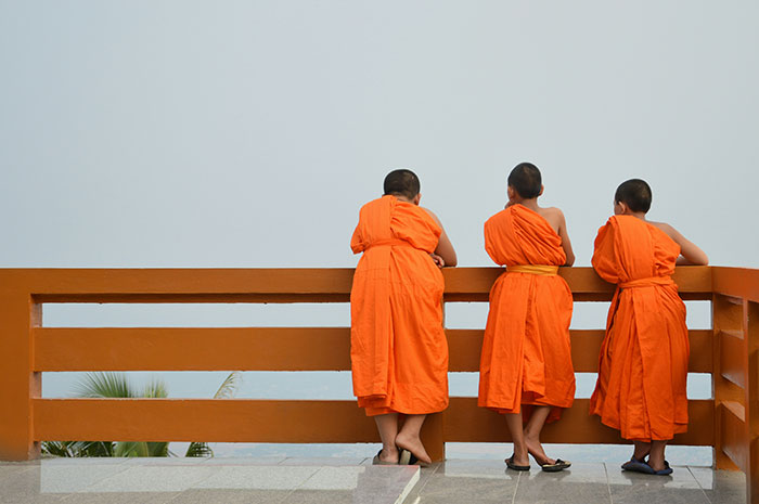 Three young monks in bright orange robes standing at a railing, reflecting on moments when experts were proven wrong.
