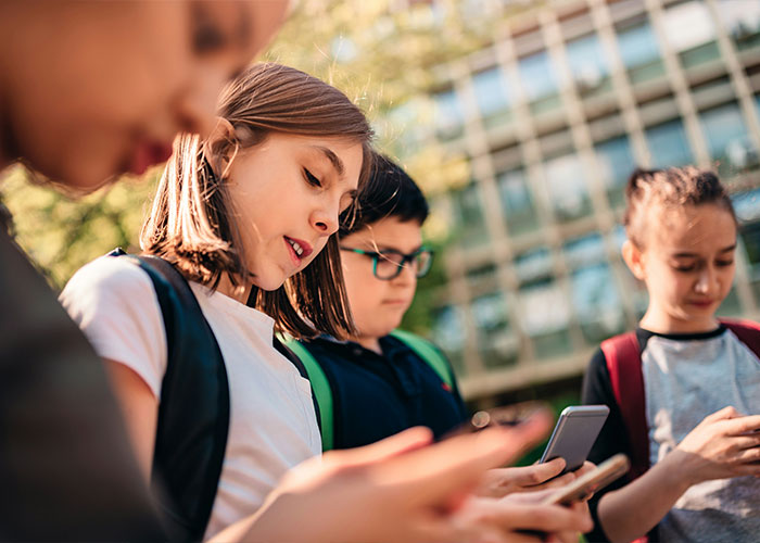 Group of young teens outdoors, focused on their smartphones, illustrating experts' views on overused slang words to banish. Group of young teens outdoors, focused on their smartphones, illustrating experts' views on overused slang words to banish.