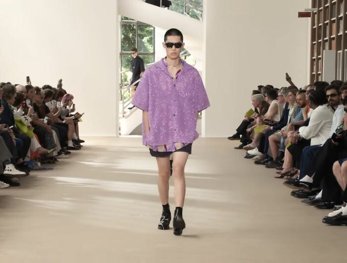 Male model walking runway in oversized purple outfit and sunglasses at Gucci fashion show, showcasing 2025 style trends.