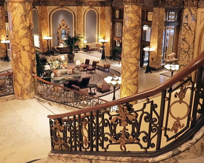 Luxurious interior of a grand historic building with marble columns and ornate wrought iron staircase railing.