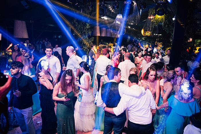 Guests socializing and dancing at an extravagant wedding celebration with colorful lights and lively atmosphere.