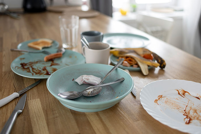 Empty plates and leftover food on a wooden table after a meal, illustrating guy eats leftovers scenario.