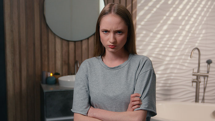 Young woman with crossed arms and frowning face, showing frustration in a modern bathroom setting about leftovers conflict.
