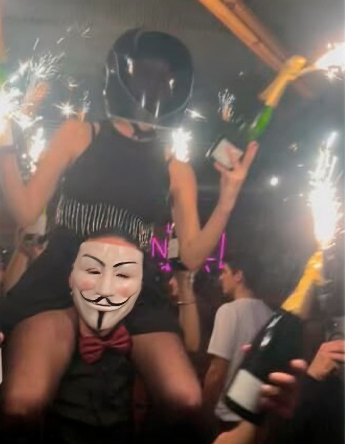 Waitress in a helmet holding sparklers and champagne bottles at a crowded party linked to the Swiss ski resort fire fate.