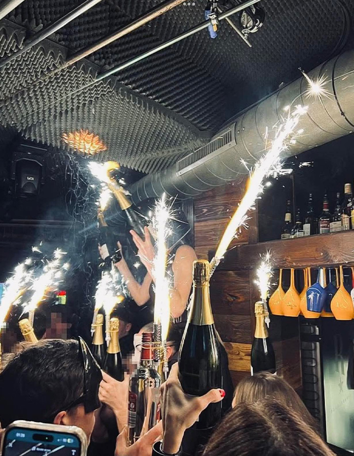 Crowd celebrating with champagne and sparklers in a lively bar scene related to Swiss ski resort fire allegations.