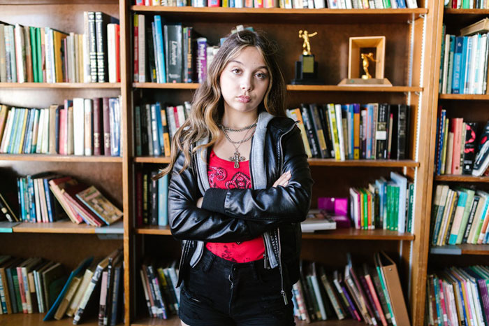 Teen girl with crossed arms standing in front of a bookshelf, reflecting on dad's claim of children being failures. Teen girl with crossed arms standing in front of a bookshelf, reflecting on dad's claim of children being failures.
