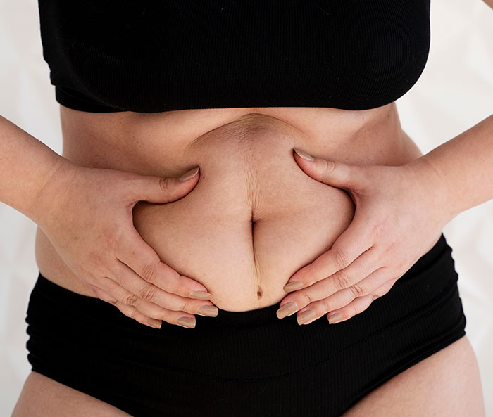 Close-up of a woman holding her stomach, highlighting real women’s bodies and body awareness topics.