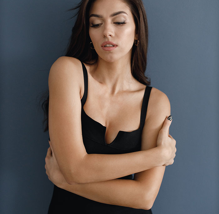 Young woman in black top with arms crossed, reflecting on women's bodies and body awareness topics.