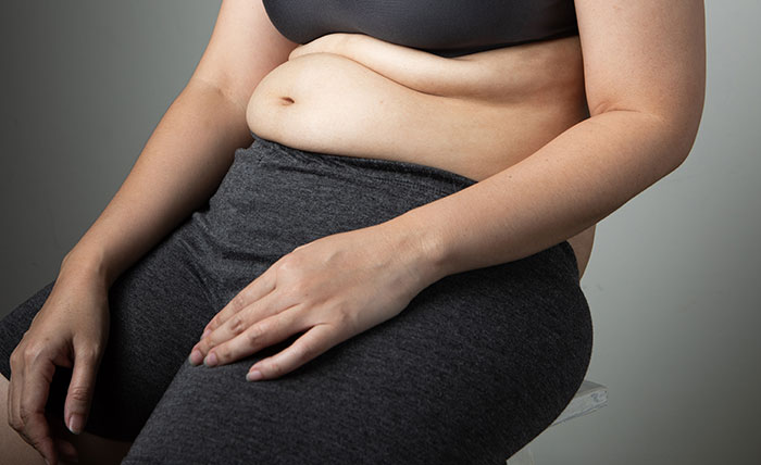 Close-up of a woman’s torso and hand showing natural body shape, highlighting women’s bodies and health awareness.