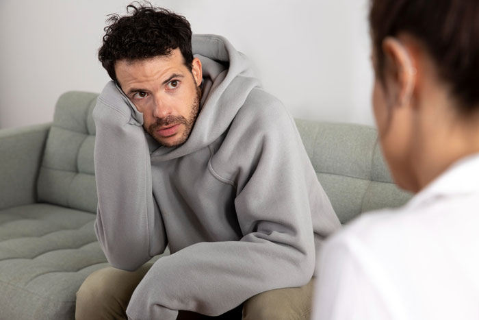 Man in a gray hoodie looking distressed while talking to a woman, illustrating issues with medicine and confidence. Man in a gray hoodie looking distressed while talking to a woman, illustrating issues with medicine and confidence.