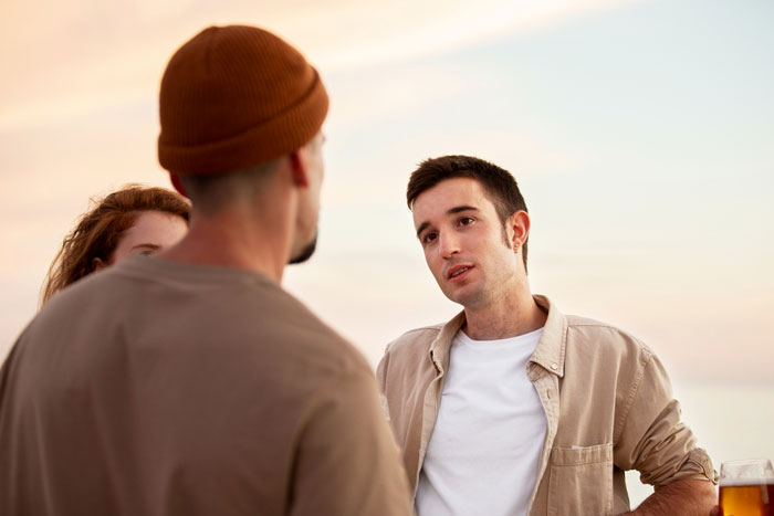 A young man discussing wedding plans and money with his friend and fiance outdoors during sunset.