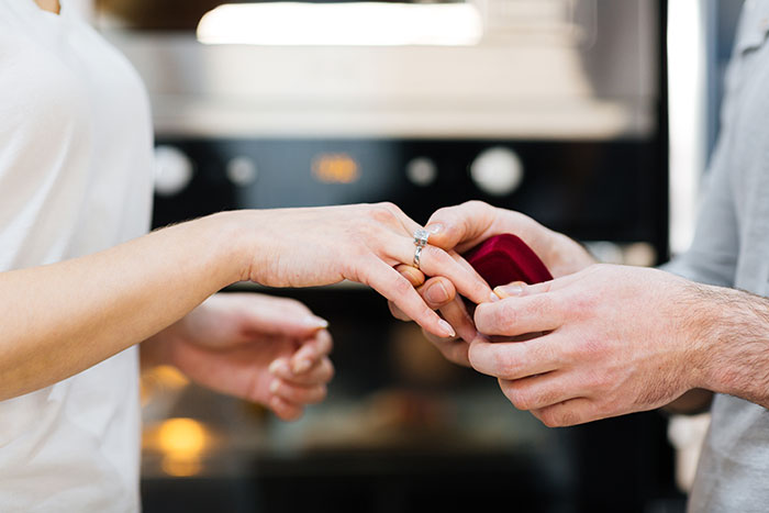Widower boyfriend taking off wedding ring while woman holds his hand during emotional moment at home.