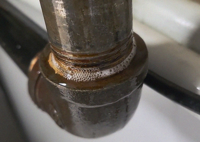 Close-up of leaking rusty pipe joint with water bubbles, illustrating common homeownership plumbing issues after buying a house.