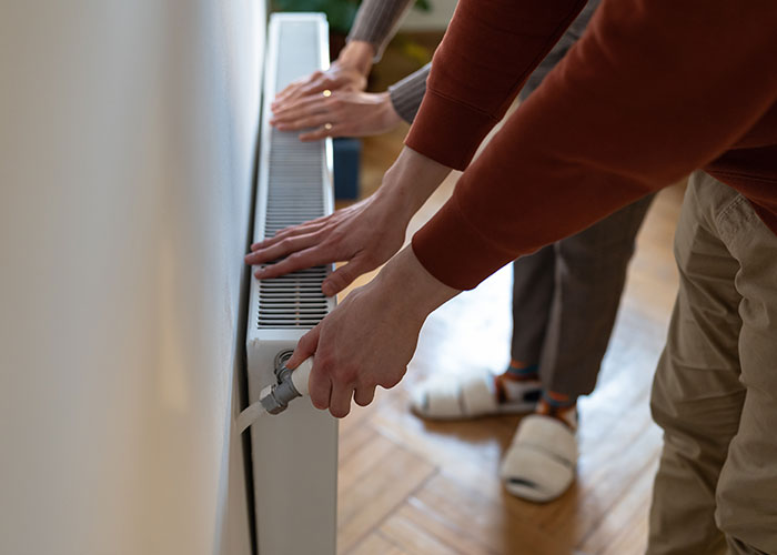 Two people inspecting a radiator valve in a home, illustrating challenges beyond buying a house.