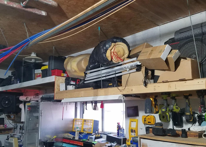Cluttered garage storage with tools, boxes, and insulation materials on shelves in a partially finished house interior.