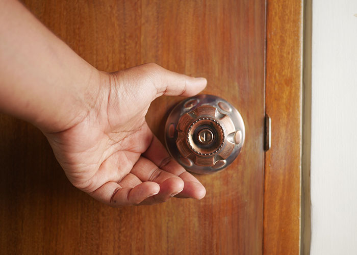 Hand gripping a round door k**b on a wooden door symbolizing the experience of buying a house and homeownership challenges.