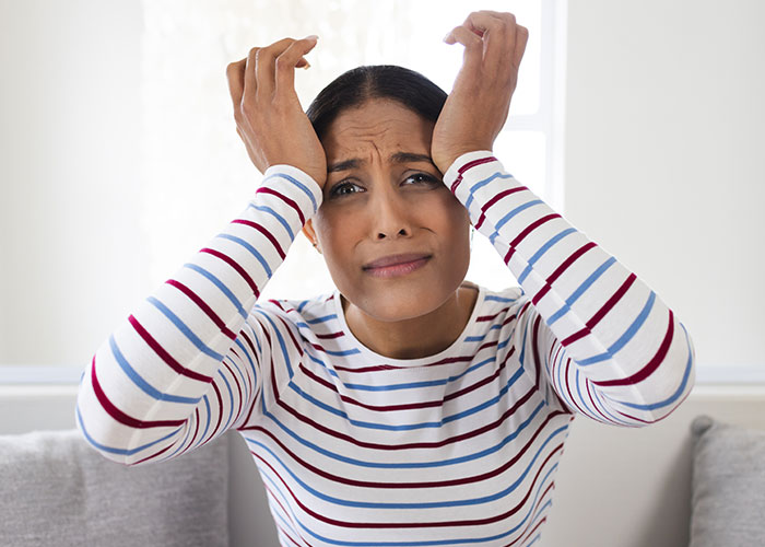 Stressed woman in striped shirt holding her head, illustrating the challenges after buying a house beyond the purchase process.