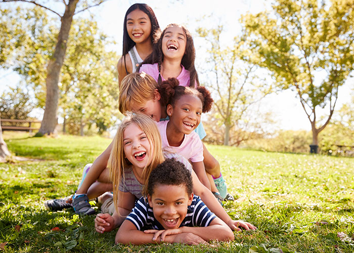Group of happy children playing and laughing outdoors in a sunny park, enjoying a warm day together.