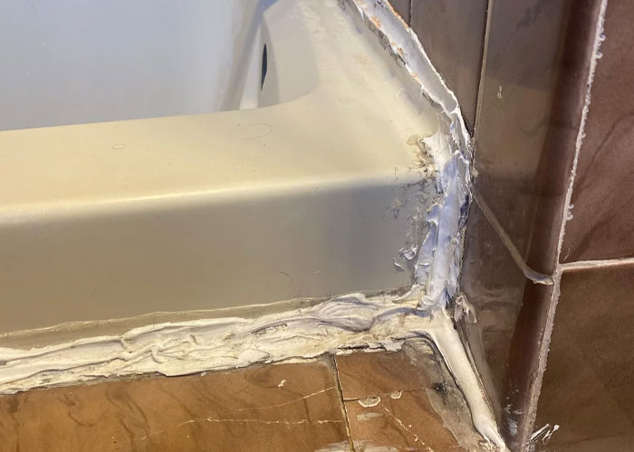 Close-up of a poorly sealed bathtub corner showing damaged caulking and tile, highlighting common homeownership challenges.