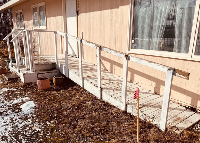 Worn wooden porch with chipped white railing on a beige house, illustrating challenges of owning a house after purchase.