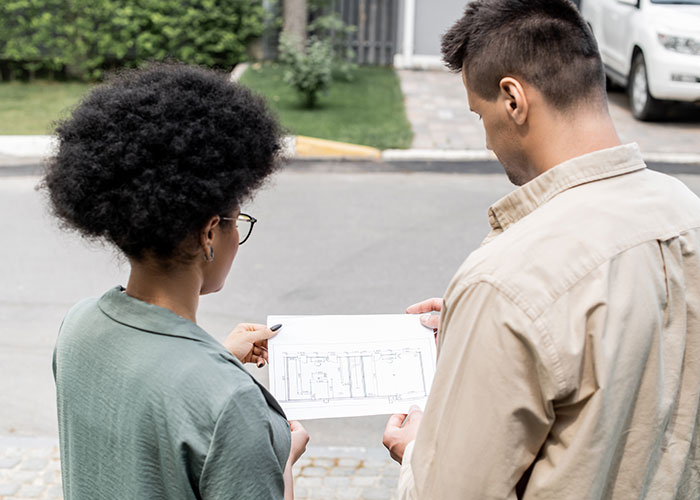 Two people reviewing house plans outside in a residential neighborhood after buying a house.