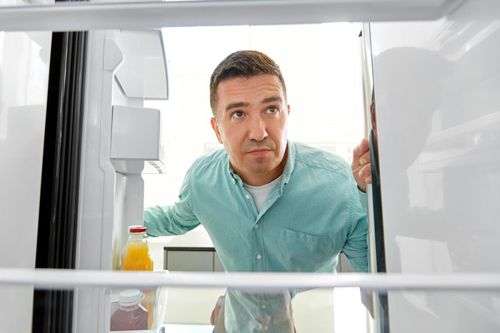 Man stealing extra-spicy lunch from office fridge, looking cautiously around before taking the food.