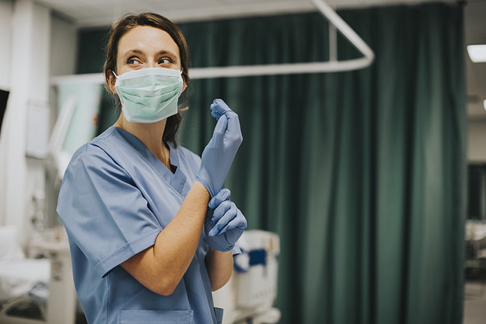 Woman in medical scrubs wearing a mask and putting on gloves, portraying a healthcare professional in a hospital setting.