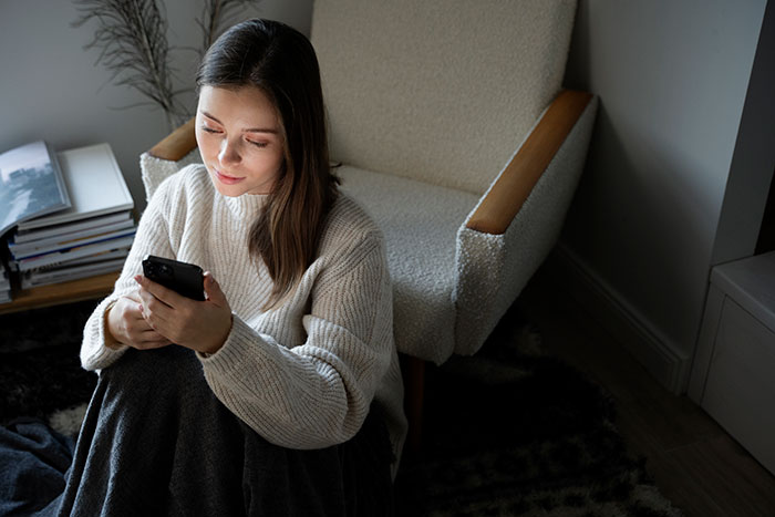 Young woman sitting indoors looking at her phone, reflecting on decisions about her career and storytelling.