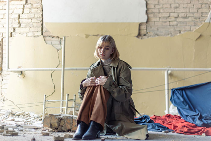 Woman sitting in a damaged room, reflecting on surgery recovery and a friend driving 1100 miles in a dirty car. - 51