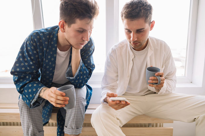 Two young men holding mugs and looking at a phone screen, illustrating friend catfishes married woman story.