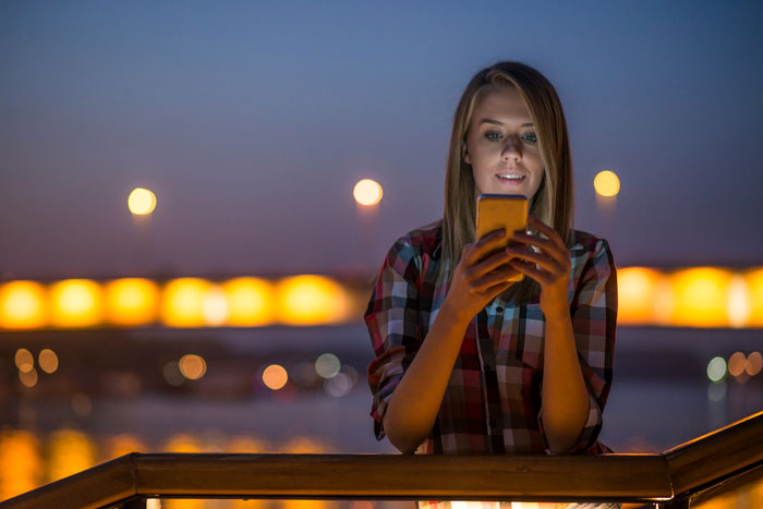 Woman using smartphone outdoors at night, illustrating friend catfishes married woman in online relationship.