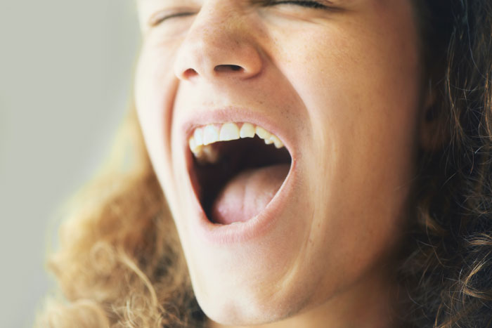 Close-up of a woman screaming with curly hair, illustrating emotions related to creepy dad and lying about theft leading to jail.