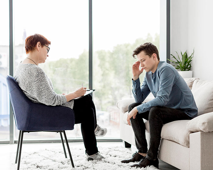 Woman taking notes while talking to a man who looks stressed, illustrating mil refuse baby name family conflict concept.