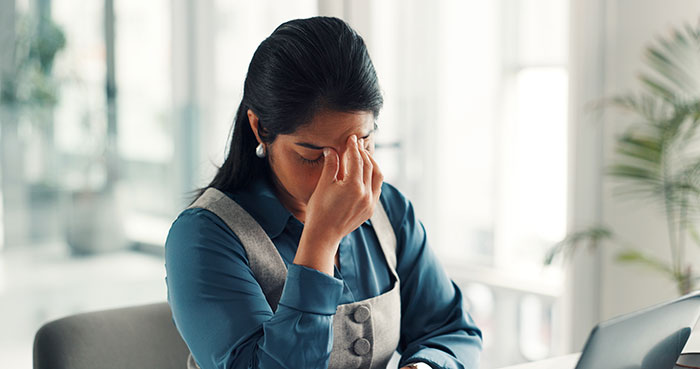 Stressed woman sitting at desk, rubbing eyes, representing estranged relatives demanding access to wedding they were never invited to.