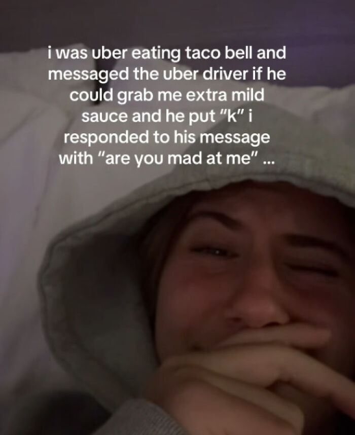 Person wearing a hooded sweatshirt laughing while reading funny and unhinged texts from Uber drivers on a phone screen.