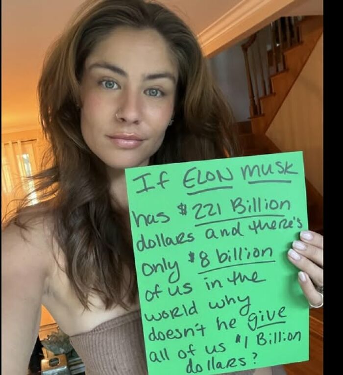 Woman holding a handwritten sign about Elon Musk's wealth, reflecting on comprehension struggles with complex statements.