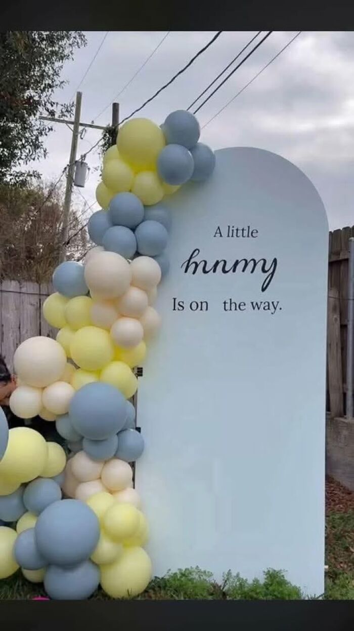 Baby shower decoration with pastel balloons and a confusing sign that challenges people trying to understand what they read.