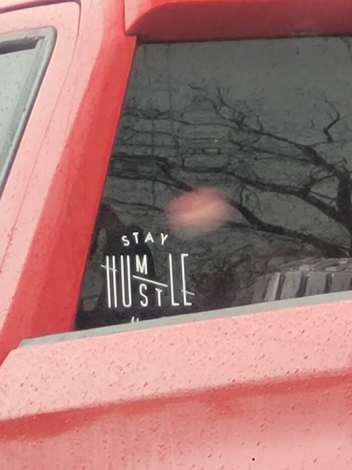 Sticker on a red car window with a confusing text design that breaks the brain trying to understand what it reads.