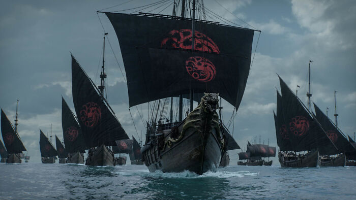 Fleet of ships with black sails and red dragon sigils sailing on a dark sea from Knight of the Seven Kingdoms timeline.
