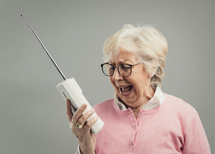 Elderly woman in pink sweater angrily shouting into a vintage mobile phone, representing Gen Z male Karen concept. Elderly woman in pink sweater angrily shouting into a vintage mobile phone, representing Gen Z male Karen concept.