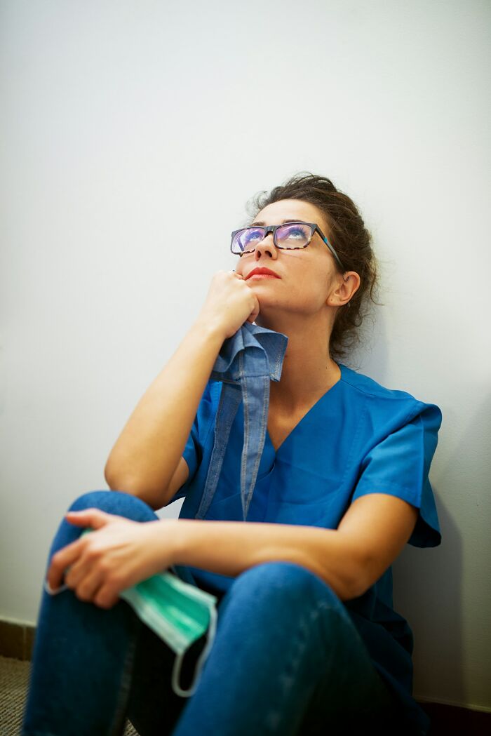 Woman in medical scrubs sitting on floor looking up thoughtfully, reflecting on unexplainable medical events and prognosis.