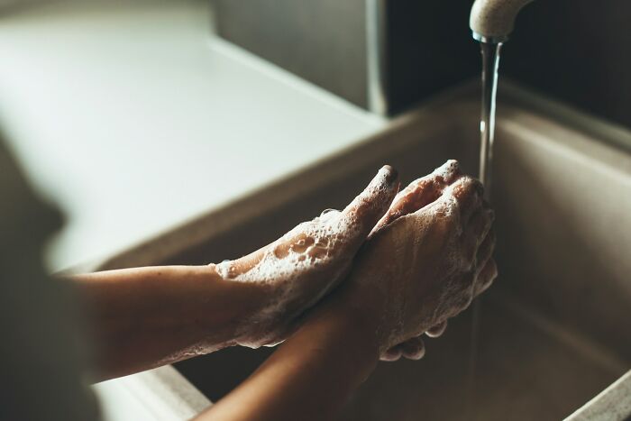 Person washing hands with soap under running water, highlighting daily dangers from common exposure and hygiene risks.