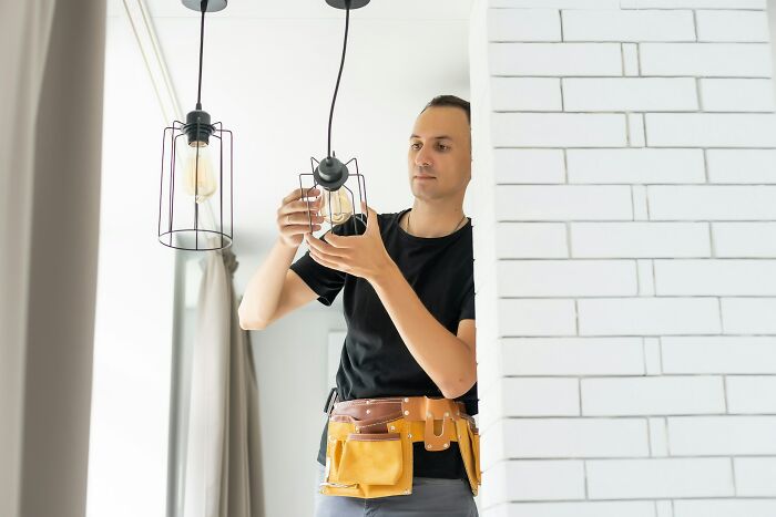 Man with tool belt installing modern lights indoors, showcasing practical intelligence and problem-solving skills.
