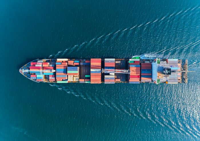 Aerial view of a cargo ship loaded with colorful shipping containers sailing on deep blue ocean water.