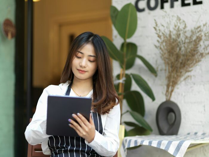 Young woman with striped apron using tablet indoors, showcasing intelligence and focus in a casual coffee shop setting.