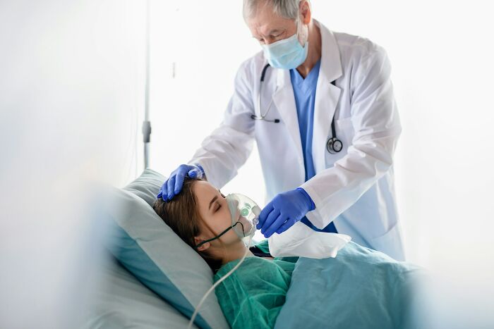 Hospital workers doctor adjusts oxygen mask for female patient lying in a hospital bed